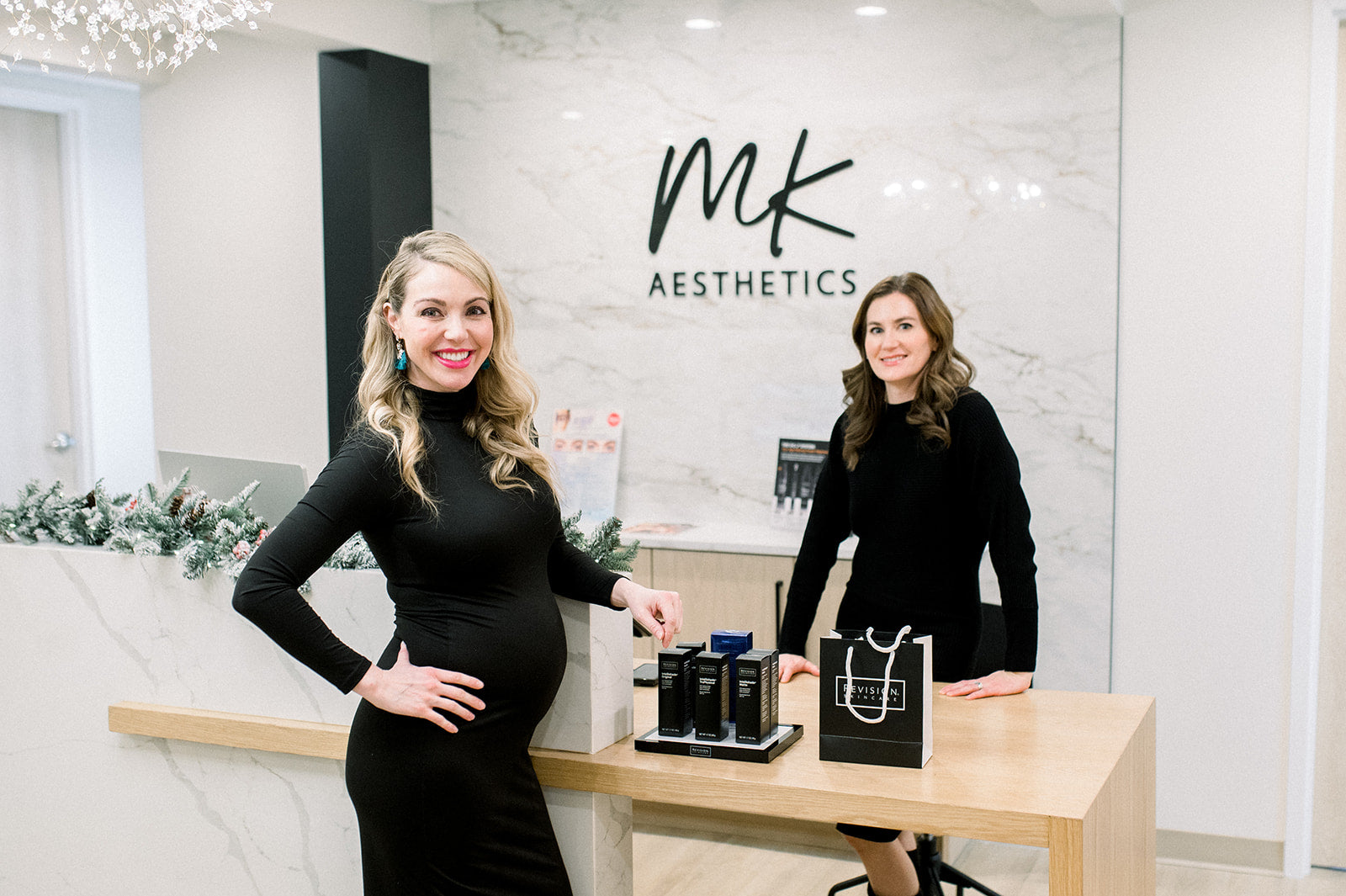 Two women at MK Aesthetics Minnetonka's med spa reception with skincare products displayed on the counter.