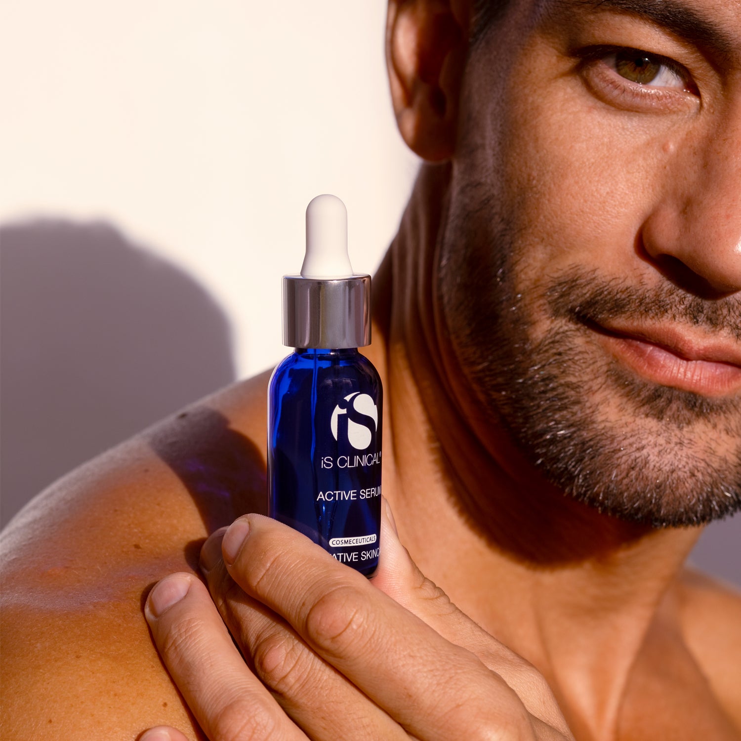 Close-up of a man holding IS Clinical Active Serum bottle, showcasing its skincare benefits.