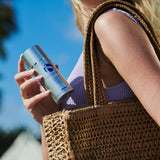 Model holding Eclipse SPF 50+ sunscreen near a stylish bag, perfect for outdoor activities.