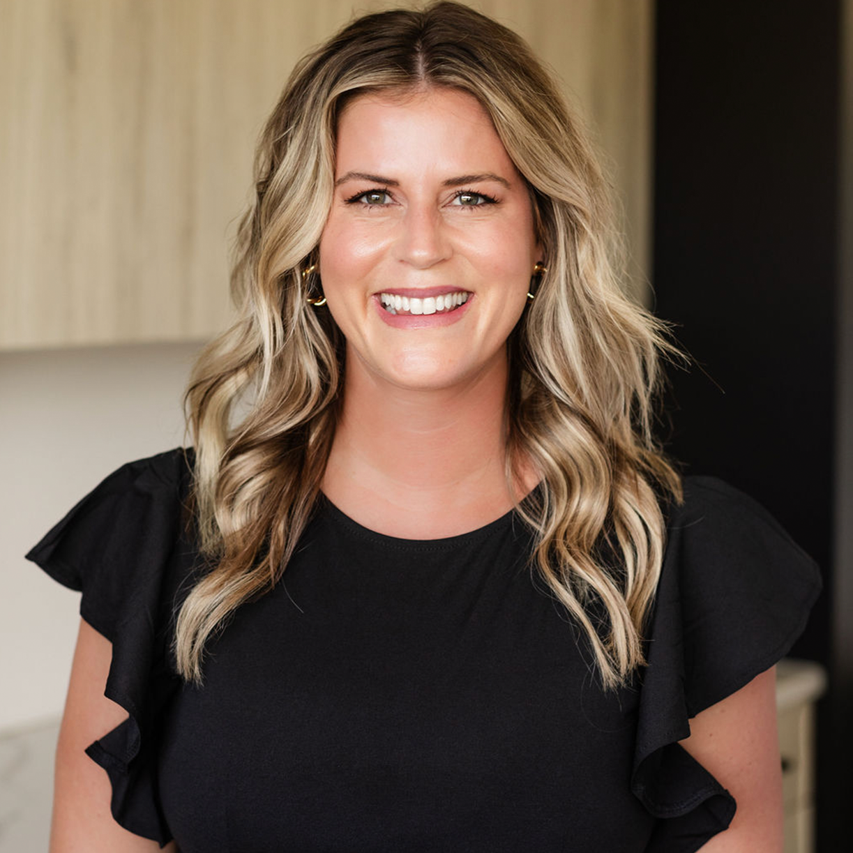 Smiling woman with long hair in a black top, representing MK Aesthetics Med Spa in Minnetonka.