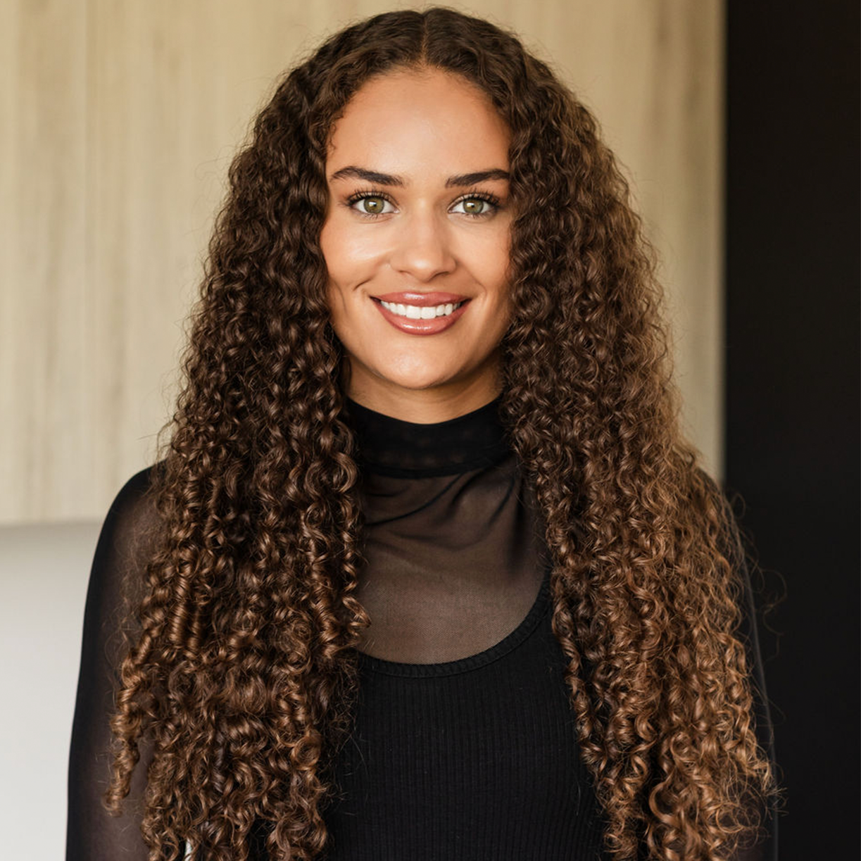 Smiling woman with curly hair in a black top at MK Aesthetics Minnetonka, a Med Spa, showcasing friendly atmosphere.